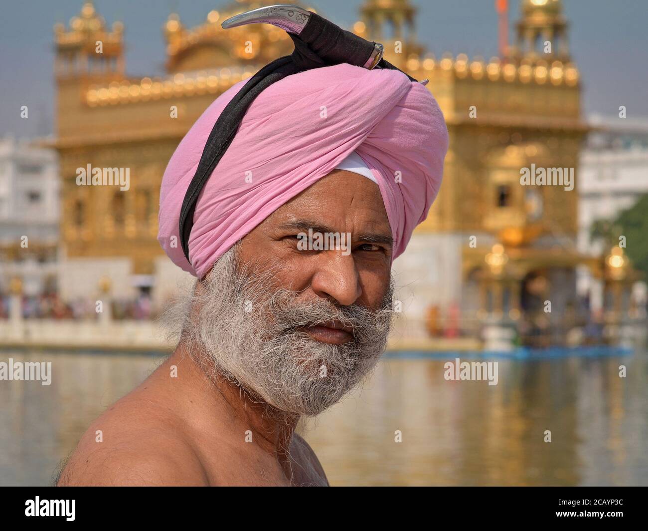 Der ältere indische Sikh-Anhänger bereitet sich auf ein Bad im heiligen „Teich des Nektars“ rund um den Goldenen Tempel vor und sichert seinen Dolch auf seinem Turban. Stockfoto