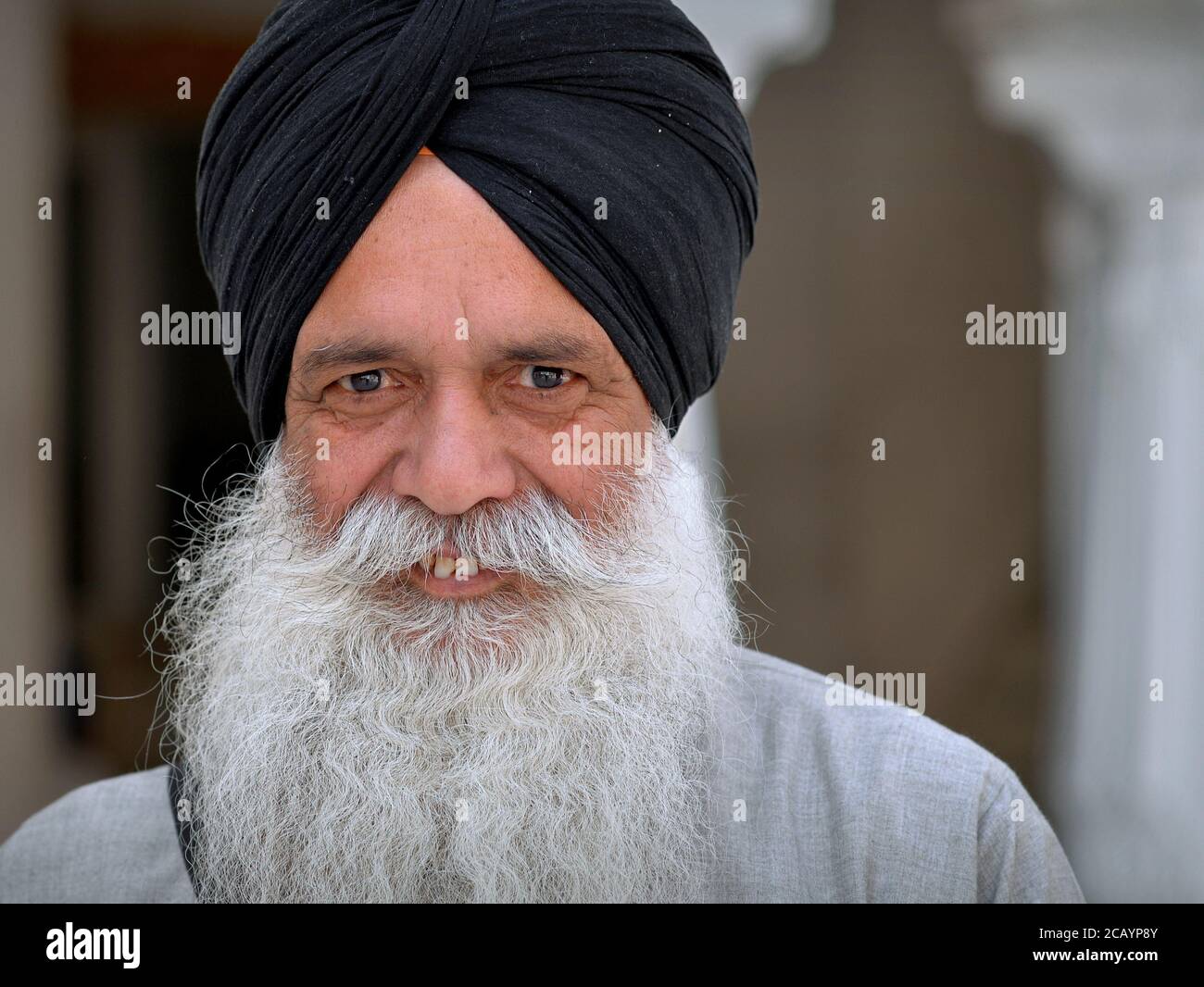 Älterer indischer Sikh-Anhänger mit weißem Bart und lächelnden Augen trägt einen schwarzen Turban (dastar) und schaut in die Kamera. Stockfoto