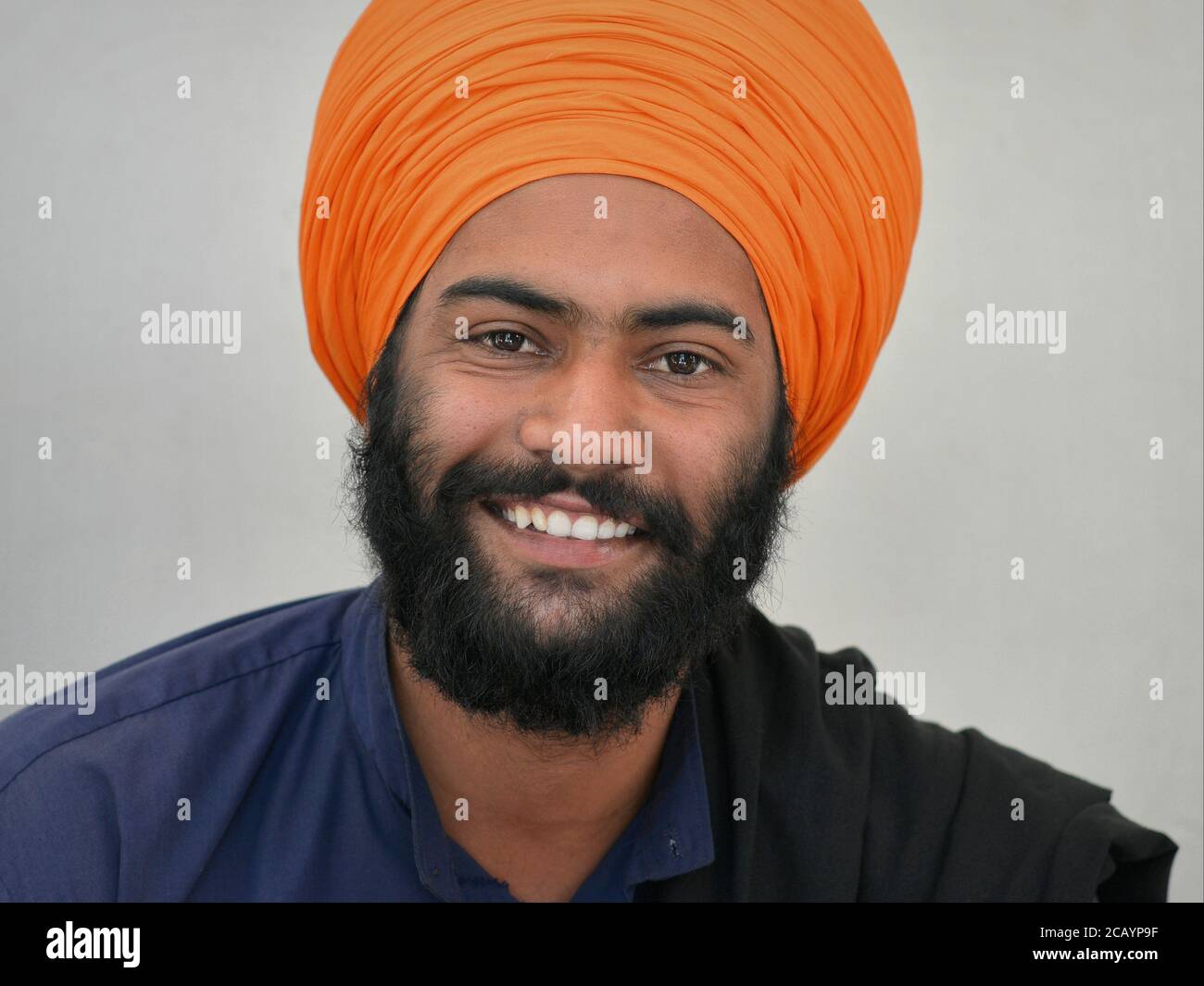 Hübscher junger indischer Sikh-Anhänger mit schwarzem Bart und lächelnden Augen trägt einen orangefarbenen Turban (dastar) und blickt in die Kamera. Stockfoto