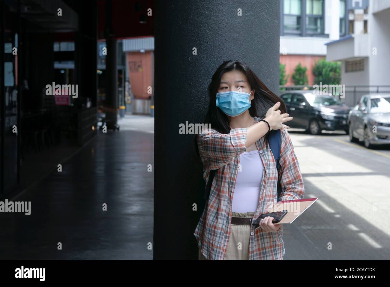 Asiatische Frau trägt Gesichtsmaske lehnt sich auf Gebäude Strahl und Berühren Sie ihr Haar Stockfoto