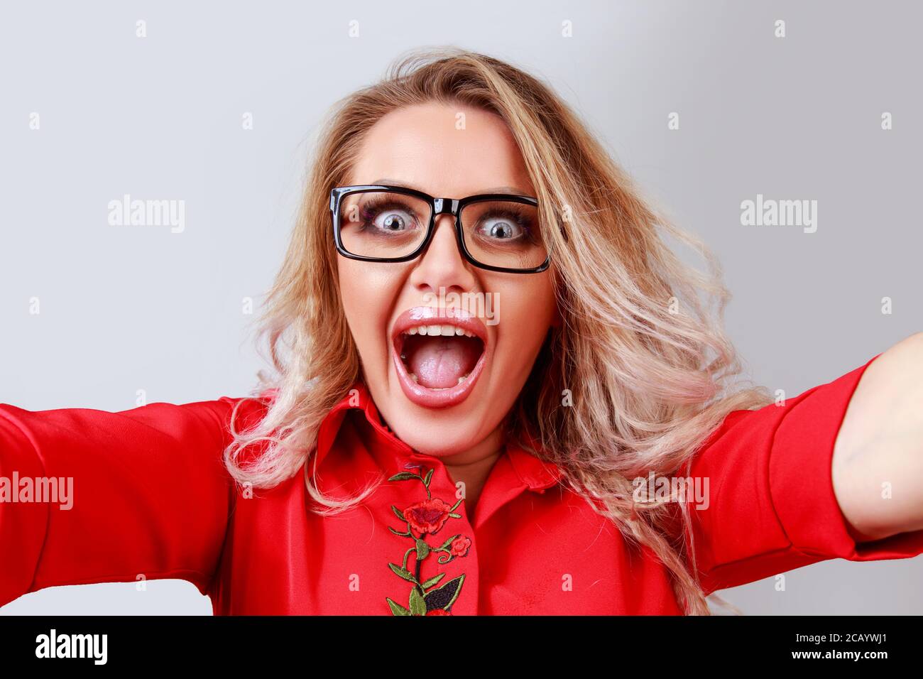 Aufgeregt blonde Frau in einer Brille mit weit geöffneten Augen und Mund geöffnet, Selfie und Blick auf die Kamera auf grauem Hintergrund. Stockfoto