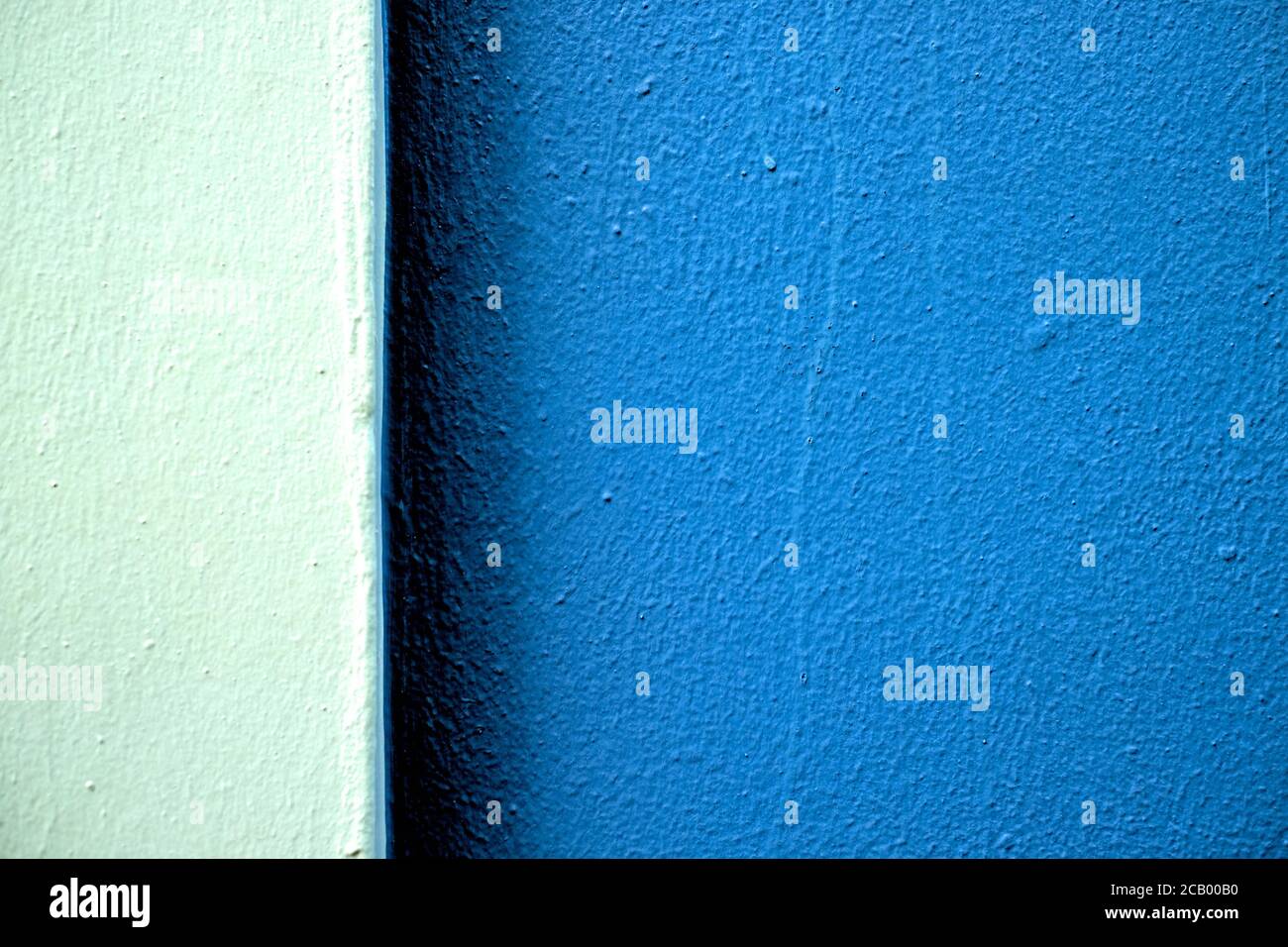 Zwei Töne von blauen Farbbändern auf einer frisch bemalten Wand in hartem Licht, versetzt mit großem dunkleren Teil. Stockfoto