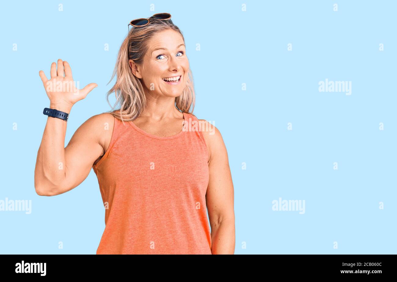 Mittelalter fit blonde Frau trägt lässige Sommerkleidung und Sonnenbrille waiving sagen Hallo glücklich und lächelnd, freundliche Willkommensgeste Stockfoto