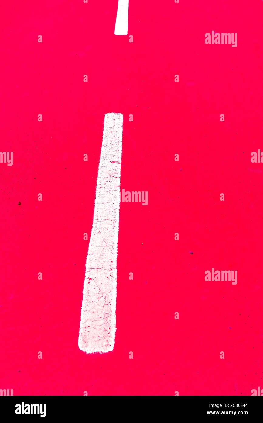 Weiße gestrichelte Linie auf lebhaft roten Hintergrund, mit Leuchtfarbe gemalt, Fahrrad Fahrbahnmarkierungen, Blitzgerät Kunstlicht. Stockfoto