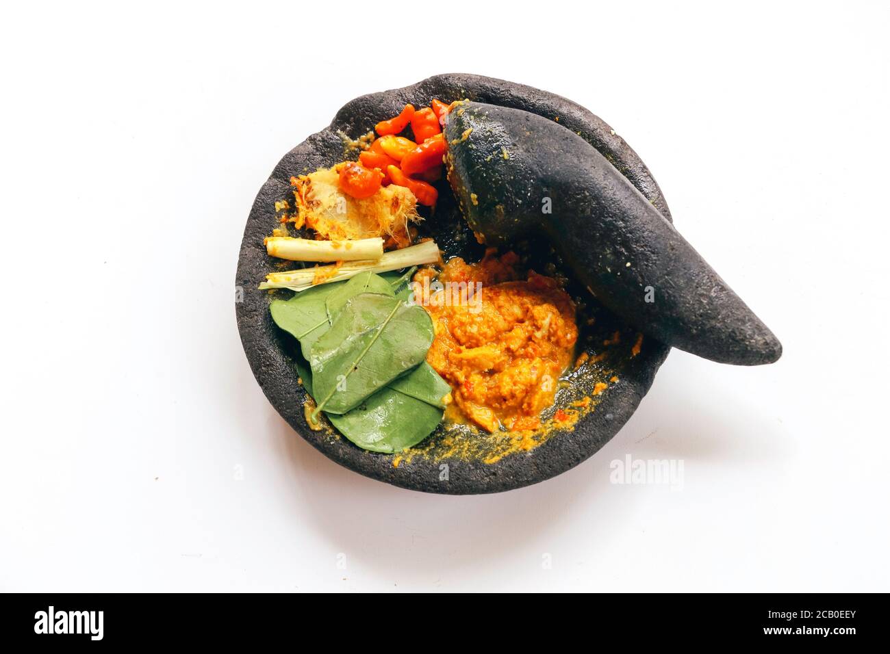 Traditioneller Steinmörtel und Stößel aus Asien mit würzigen Zutaten Chili, gelbe Würze, Blatt, Leck Blatt aus Indonesien isoliert auf weißem Backgr Stockfoto