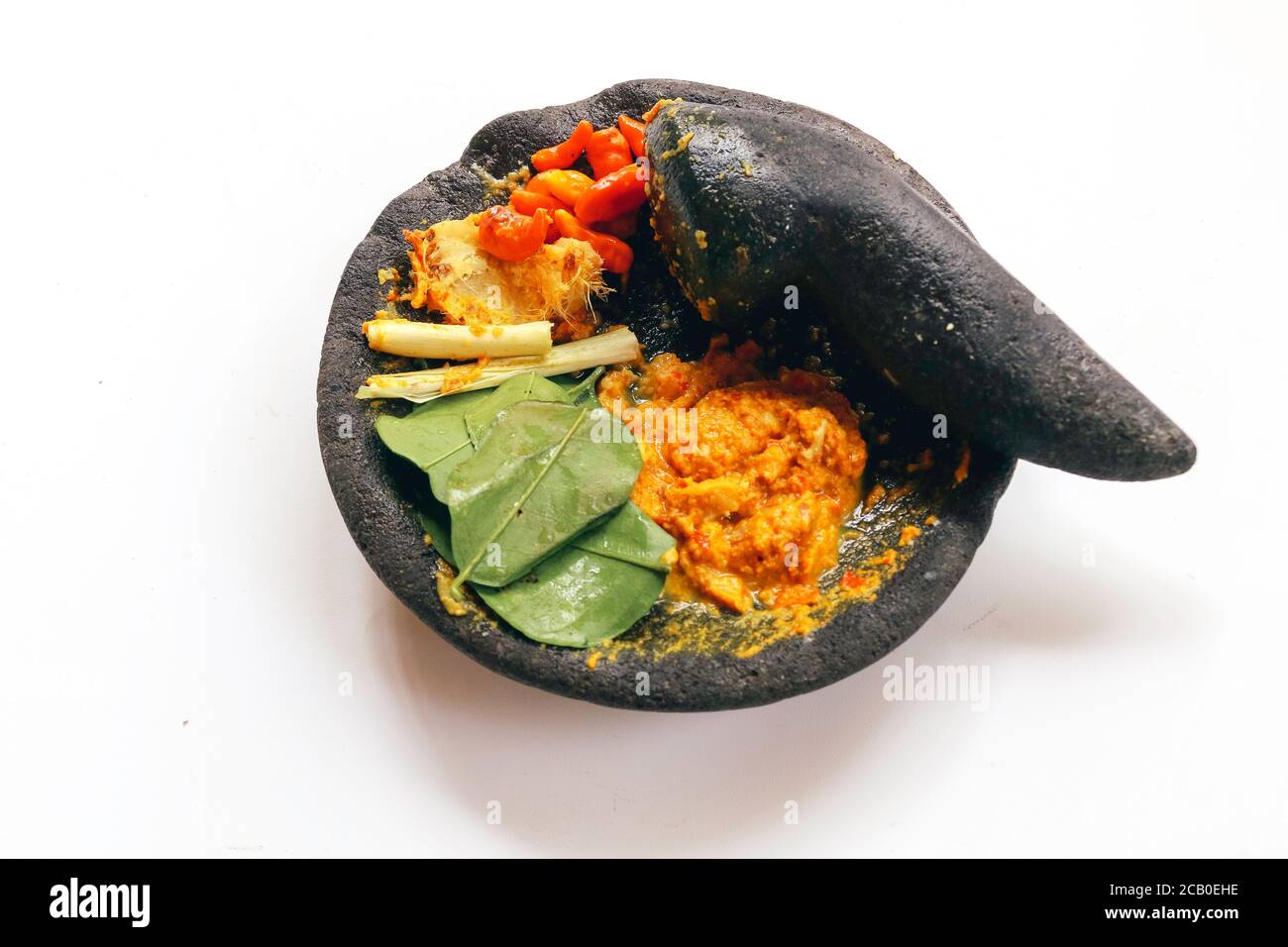 Traditioneller Steinmörtel und Stößel aus Asien mit würzigen Zutaten Chili, gelbe Würze, Blatt, Leck Blatt aus Indonesien isoliert auf weißem Backgr Stockfoto