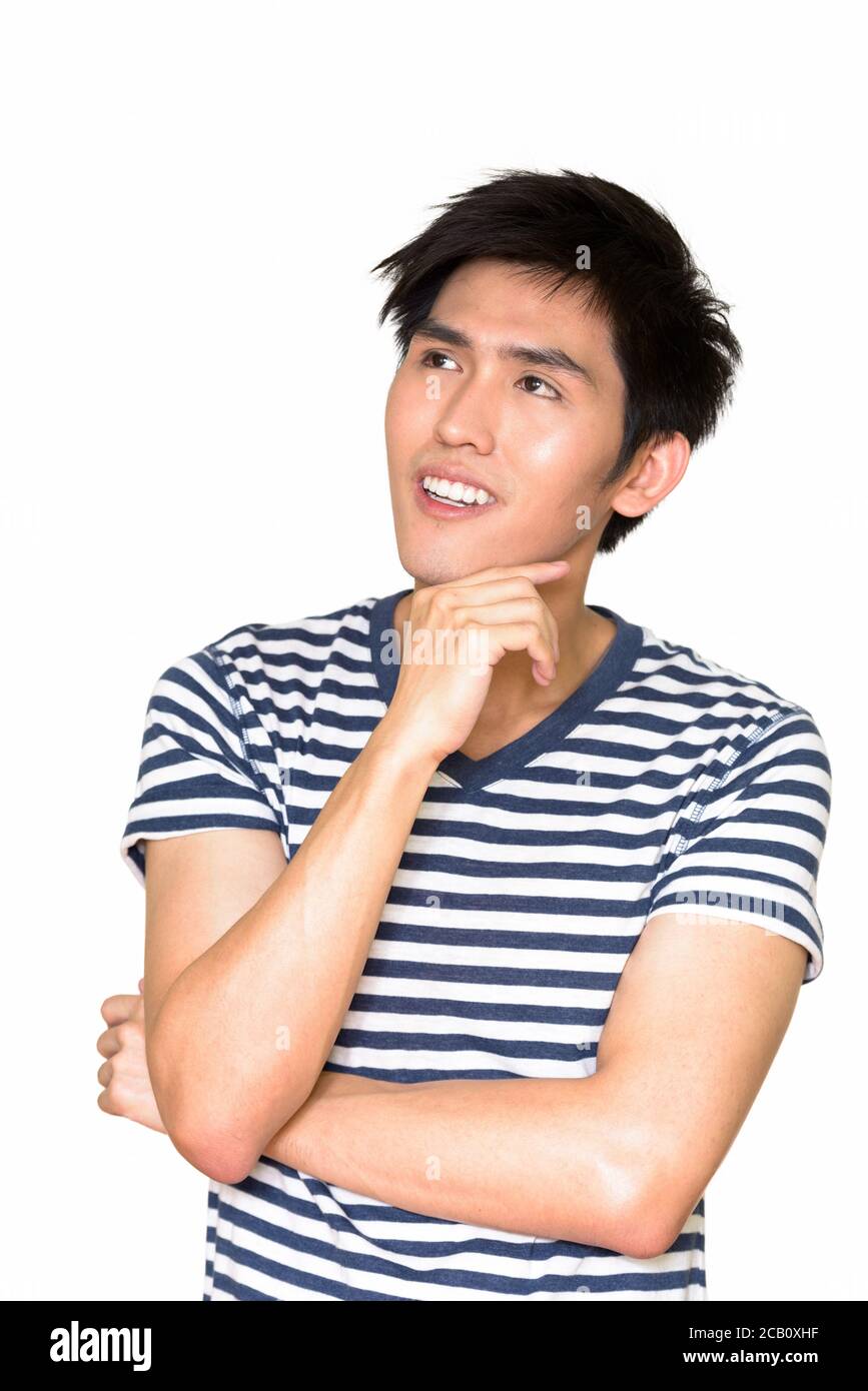 Studioaufnahme eines jungen glücklichen asiatischen Mannes, der gegen Weiß denkt Hintergrund Stockfoto