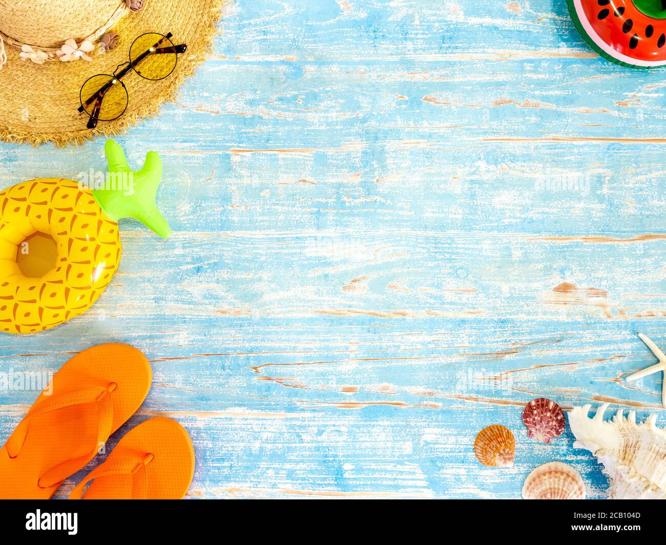 Farbenfrohe Strandaccessoires, Muscheln, Strohhut, Sonnenbrille, orangefarbene Flip Flops und belüftter Strandball auf vintage blauem Holzbrett mit Platz. Reisen Stockfoto