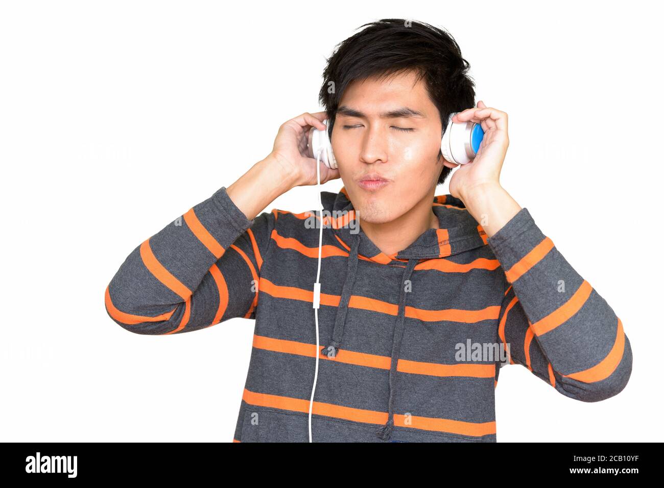 Studioaufnahme des jungen hübschen asiatischen Mannes, der Musik mit hört Kopfhörer vor weißem Hintergrund isoliert Stockfoto