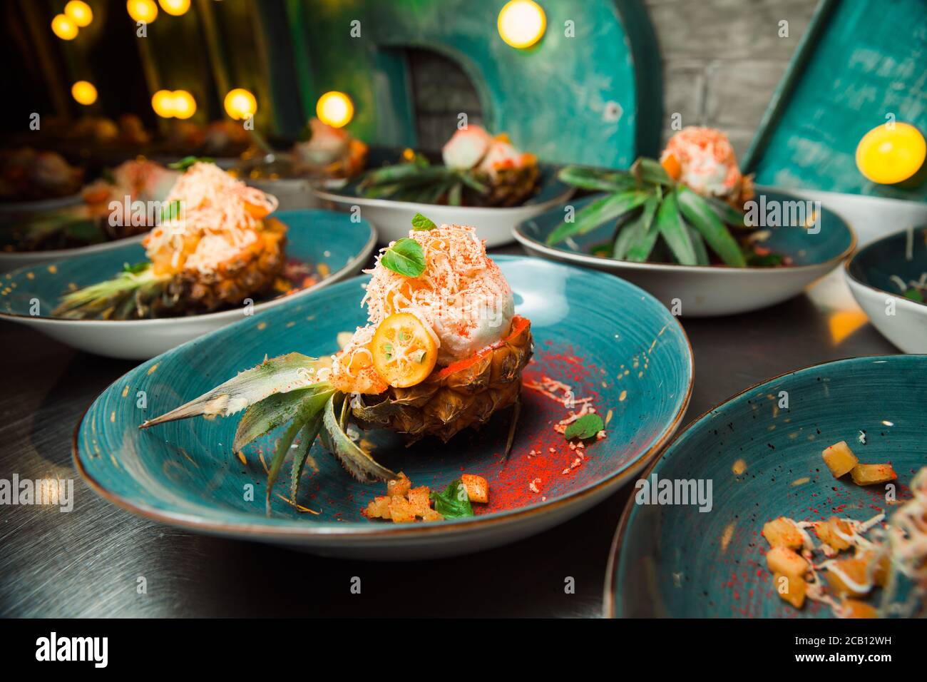 Frisch zubereiteter Salat liegt in der Ananas, die längs geschnitten und mit geriebenem Käse bestreut wird. Alles sieht sehr appetitlich aus. Stockfoto
