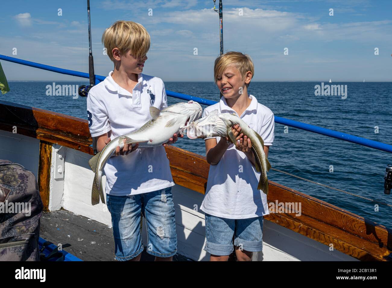 Malmö, Schweden - 6. August 2020: Zwei Jungen zeigen auf einem Familienanglerausflug ihren frischen Kabeljau-Fang. Blauer Ozean und Himmel im Hintergrund Stockfoto
