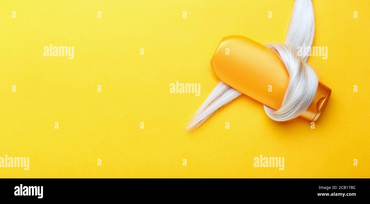 Shampoo-Flasche in Sperre von blonden Haaren auf orangefarbenem Hintergrund gewickelt. Gold Flasche Shampoo in gefärbten Haar Strang. Haarpflege Kosmetik Bad Schönheit Stockfoto