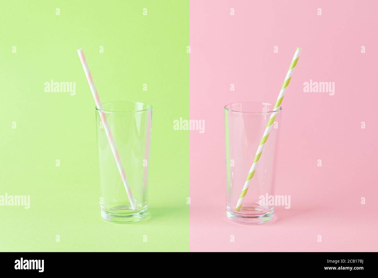 Leeres, hohes Glas mit einem rosa Trinkhalm aus Papier auf grünem Hintergrund und einem weiteren mit einem grünen Trinkhalm aus Papier auf pinkem Hintergrund. Stockfoto
