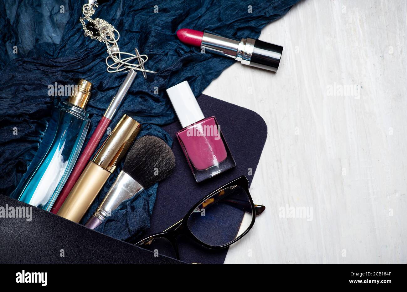 Verschiedene Make-up und kosmetische Produkte fallen aus einer weiblichen Tasche Tischplatte flach legen. Mehrere Parfüms Lippenstifte Nagellacke und Pinsel ein anderes ac Stockfoto