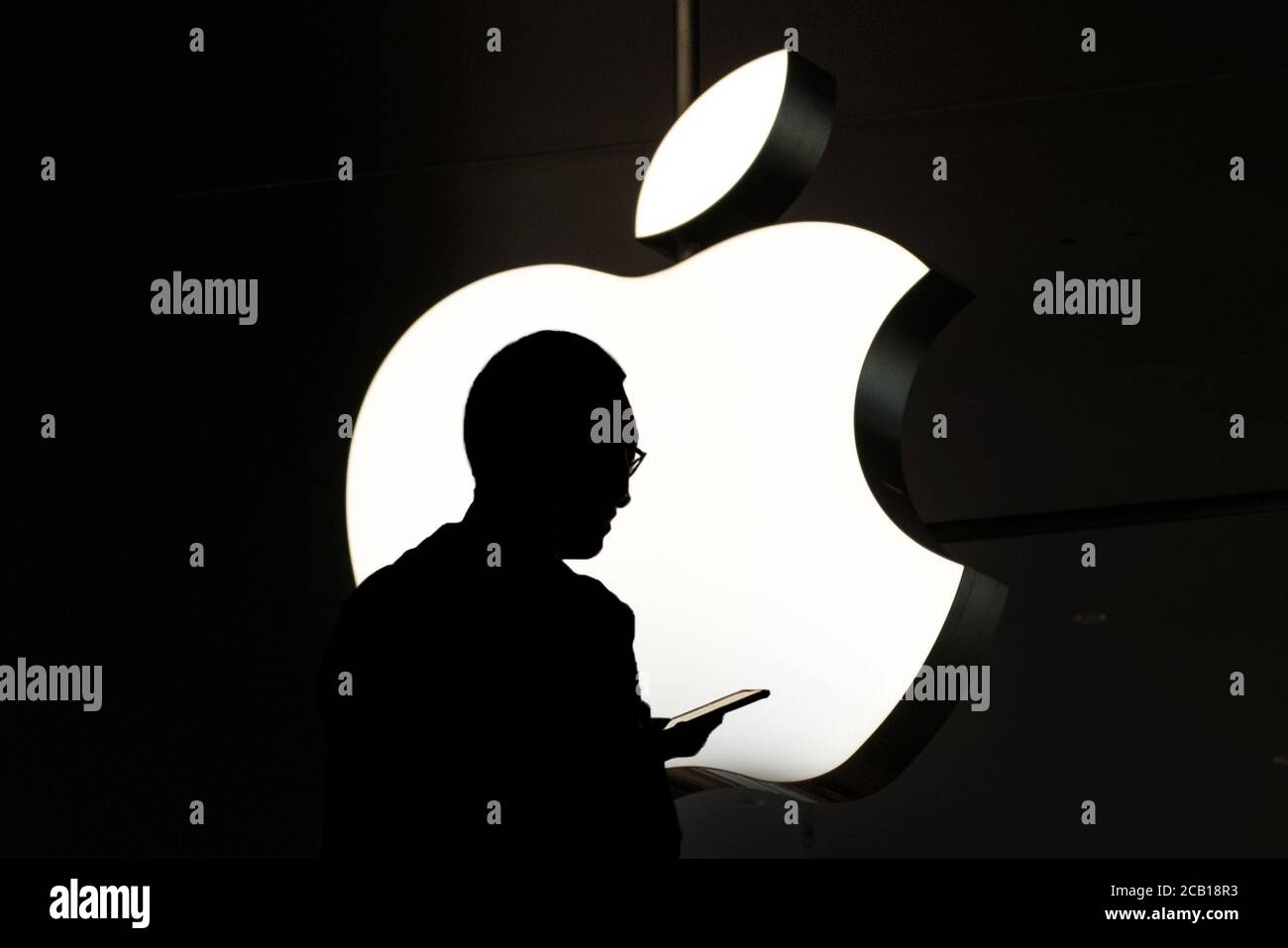 Hongkong - November, 2019: Silhouette einer Person, die das Handy vor dem Apple-Logo benutzt Stockfoto