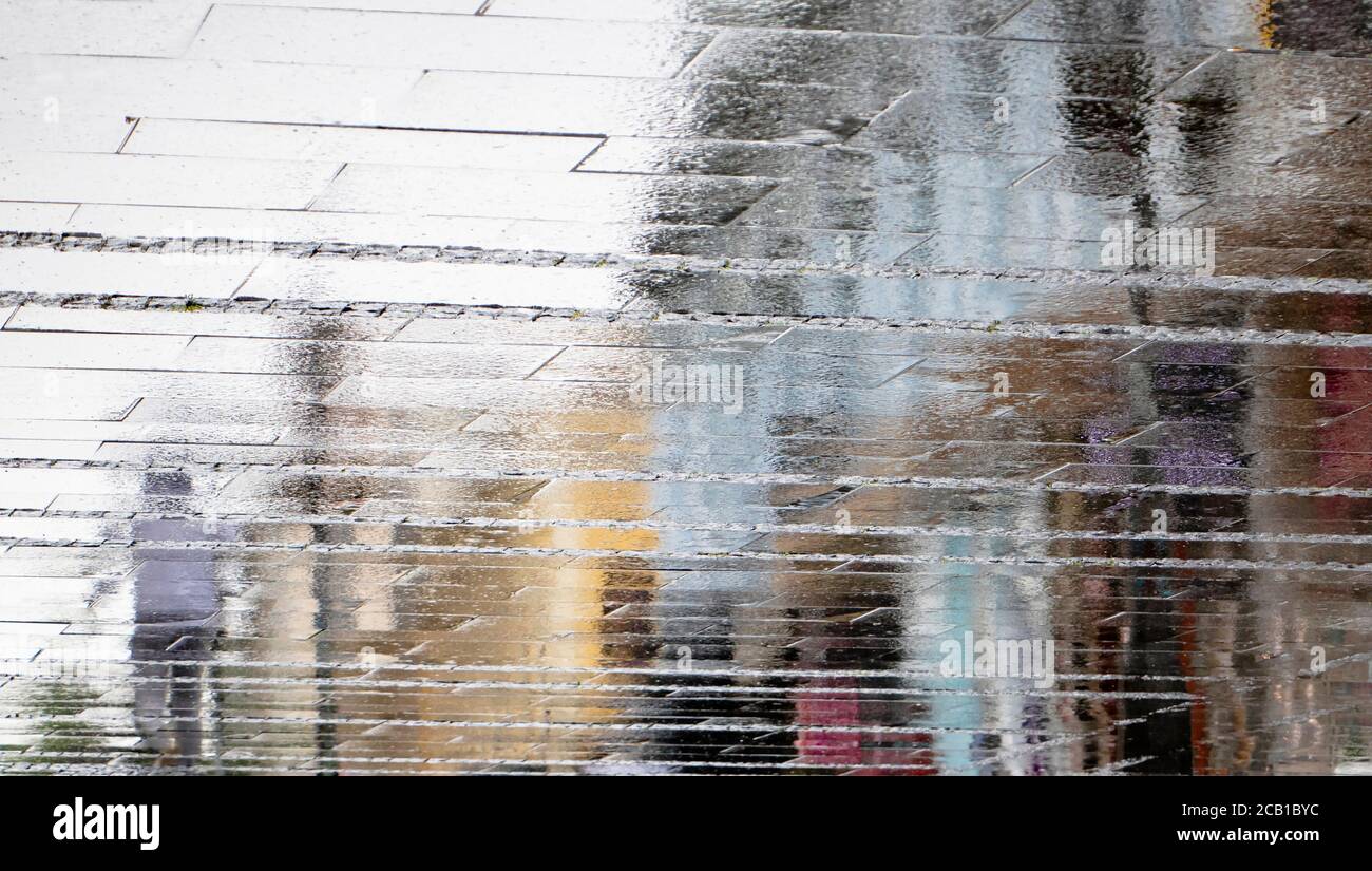 Verschwommener Spiegelschatten Silhouette auf nasser Pfütze eines Mannes, der an einem regnerischen Tag auf einer Stadtstraße läuft, abstrakter Hintergrund Stockfoto