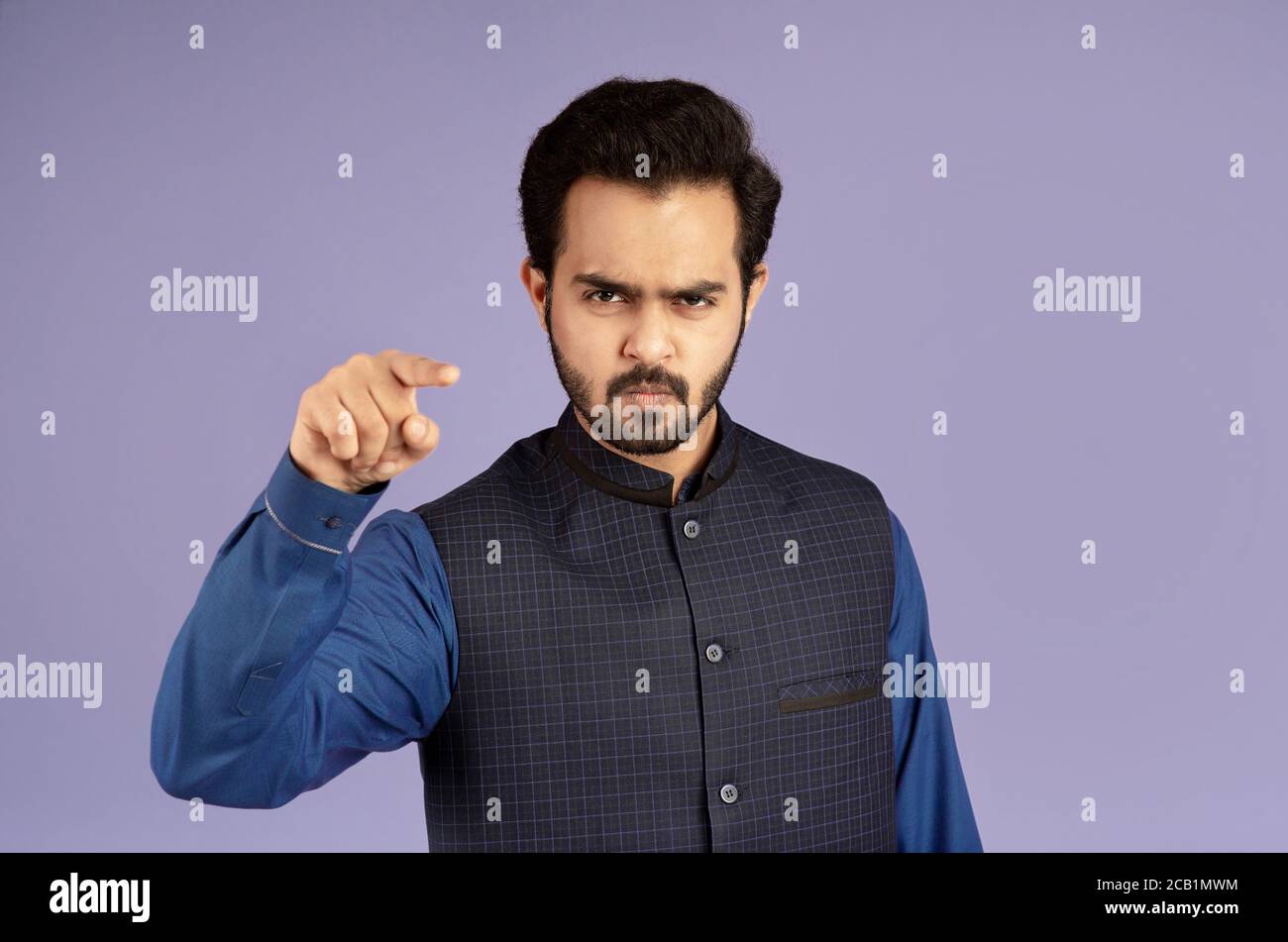 Wütend indischen Mann zeigt Finger auf Bildschirm in Anschuldigung über Violetter Hintergrund Stockfoto