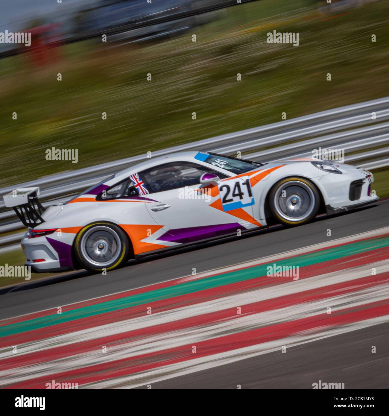 Eine Schwenkaufnahme eines weißen, orangefarbenen und violetten Rennwagens, der eine Rennstrecke fährt. Stockfoto