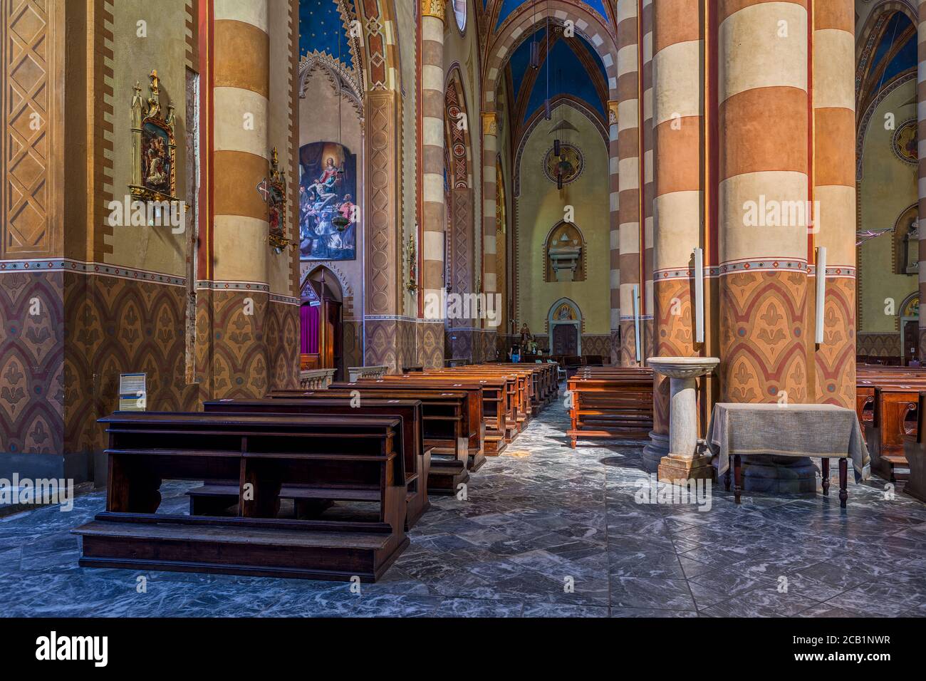 Holzbänke und Gang entlang Säulen im Inneren von San Lorenzo - eine römisch-katholische Kathedrale in Alba, Italien. Stockfoto