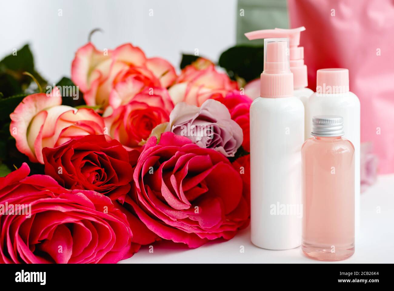 Serum, Seife, Öl auf weißem Tisch floralen Hintergrund. Blume rot rosa Rosen natürliche organische Schönheit Produkt. Spa, Hautpflege, Bad Körperbehandlung. Satz von Stockfoto