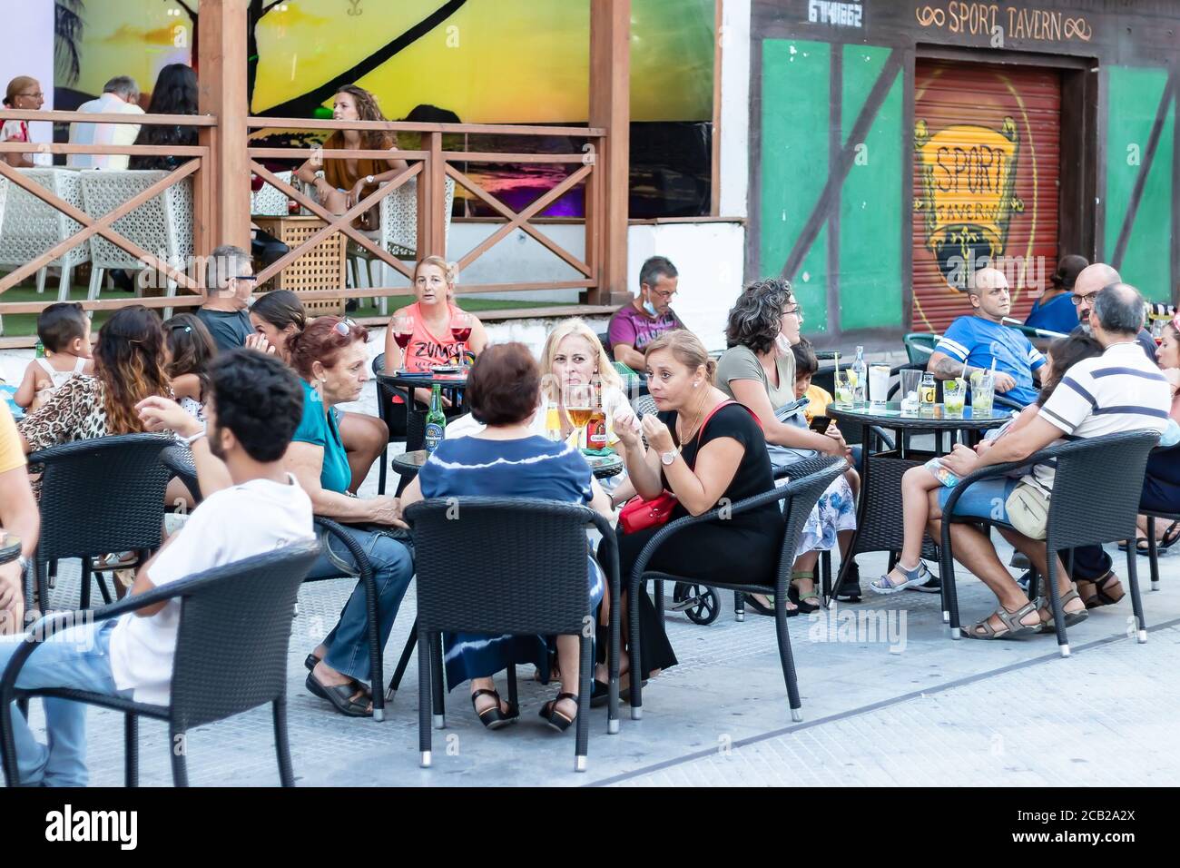 Punta Umbria, Huelva, Spanien - 7. August 2020: Die Leute, die auf der Terrasse eines Cafés und einer Bar in der Straße calle Ancha von Punta Umbria sitzen, tragen Protecti Stockfoto