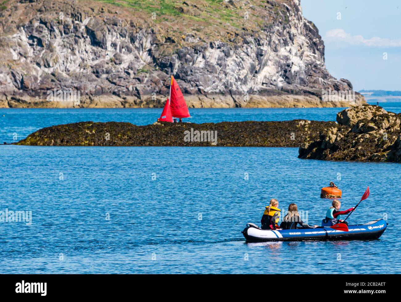 Kinder paddeln im aufblasbaren Kanu mit Segeljolle von Craiglieth Island am sonnigen Sommertag, North Berwick, East Lothian, Schottland, UK Stockfoto