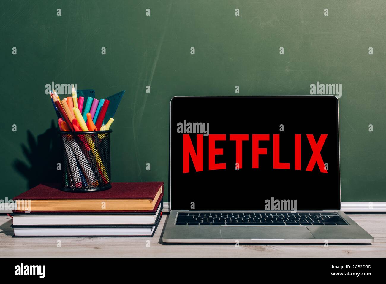 KIEW, UKRAINE - 7. JULI 2020: Laptop mit Netflix-Website in der Nähe von Stiftehalter mit Briefpapier auf Stapel von Büchern in der Nähe von grünen Kreidetafel Stockfoto