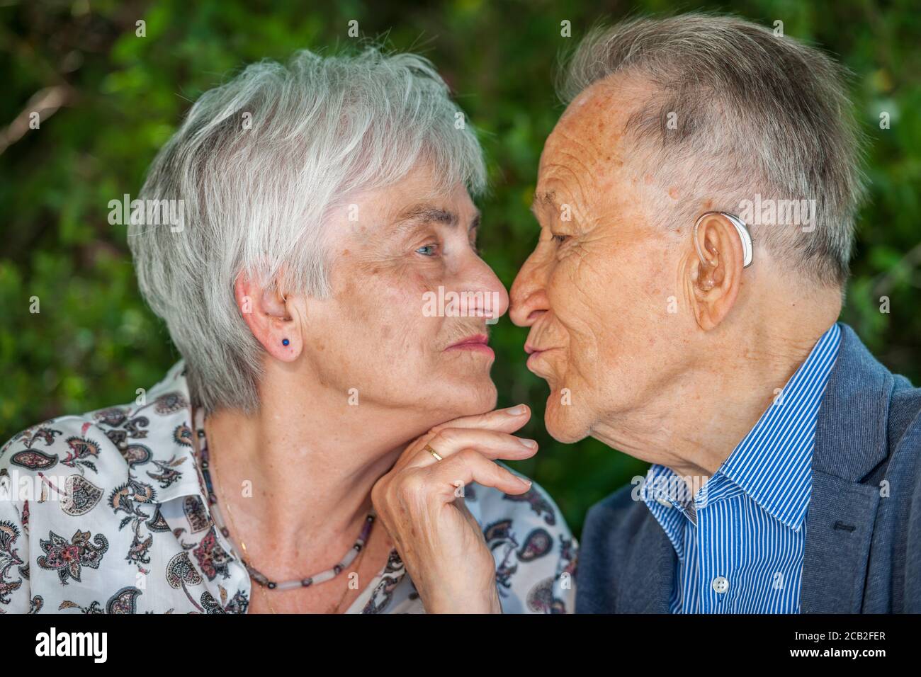 Kopf- und Schulteransicht eines küssenden älteren Rentnerpaares vor grünem verschwommenem Hintergrund. Stockfoto