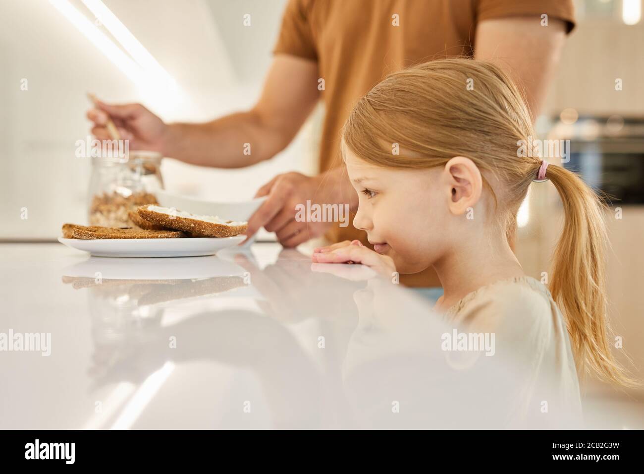 Seitenansicht Porträt von niedlichen kleinen Mädchen Blick auf leckere Sandwiches während der Wartezeit für das Frühstück in der Küche, kopieren Raum Stockfoto