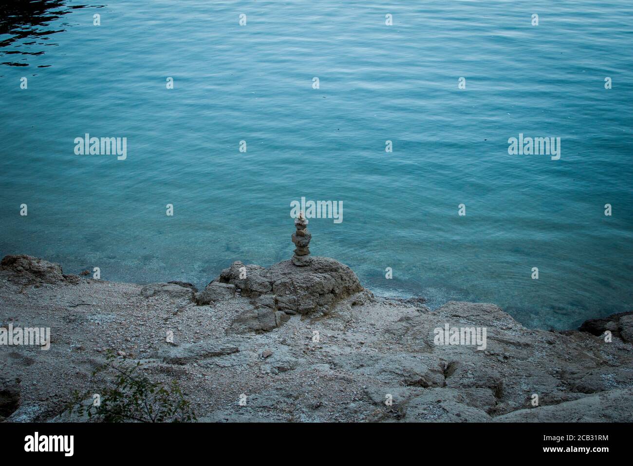 Ein Haufen Kieselsteine, der auf einem Felsen an einem Seeufer steht, mit blauem Wasser auf dem Hintergrund Stockfoto