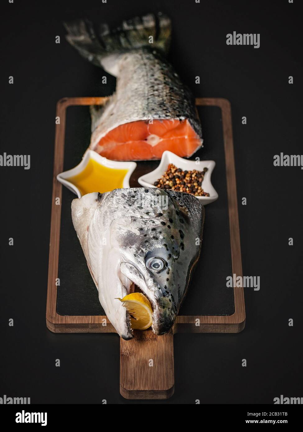 Frischer Lachs. Fischkopf und Schwanz auf einem Schneidebrett auf dunklem Hintergrund. Rote Fischsuppe mit Gewürzen, Zitrone und Olivenöl. Quelle von Nutzen OME Stockfoto