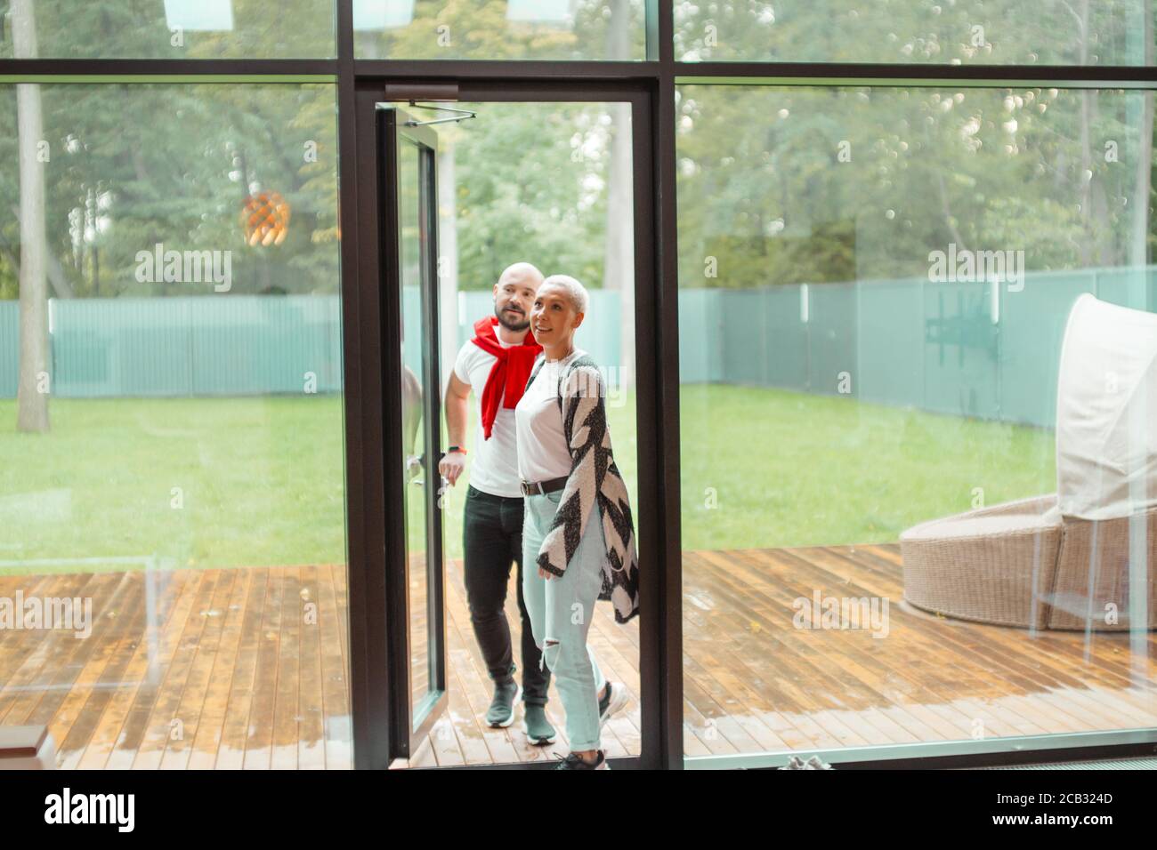 Attraktives Familienpaar betritt neues Haus, gerne Zeit hier zu verbringen. Hintergrund großes Panoramafenster Stockfoto