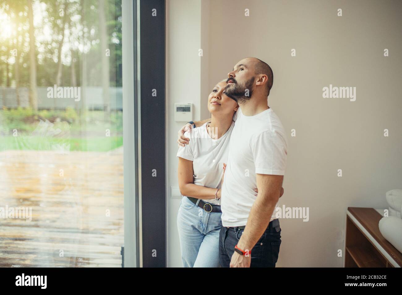 Attraktives Ehepaar im Wohnzimmer Blick durch Panoramafenster zu grünen Garten von ihrem neuen modernen Haus. Liebe, Haus, Familienkonzept Stockfoto