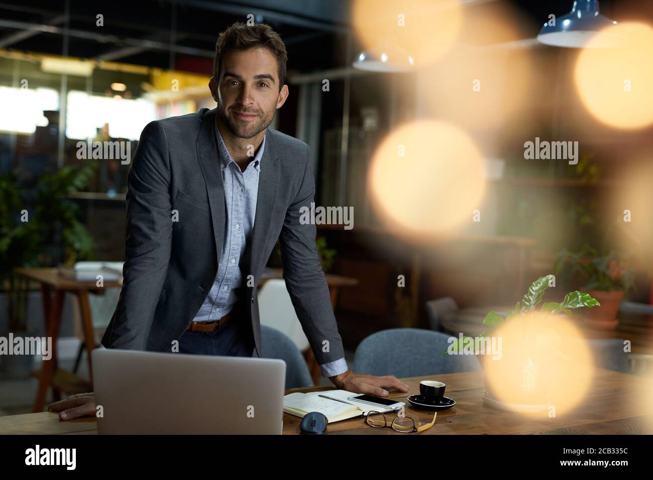Geschäftsmann, der sich nach Geschäftsschluss in einem Büro auf seinen Schreibtisch stützt Stockfoto