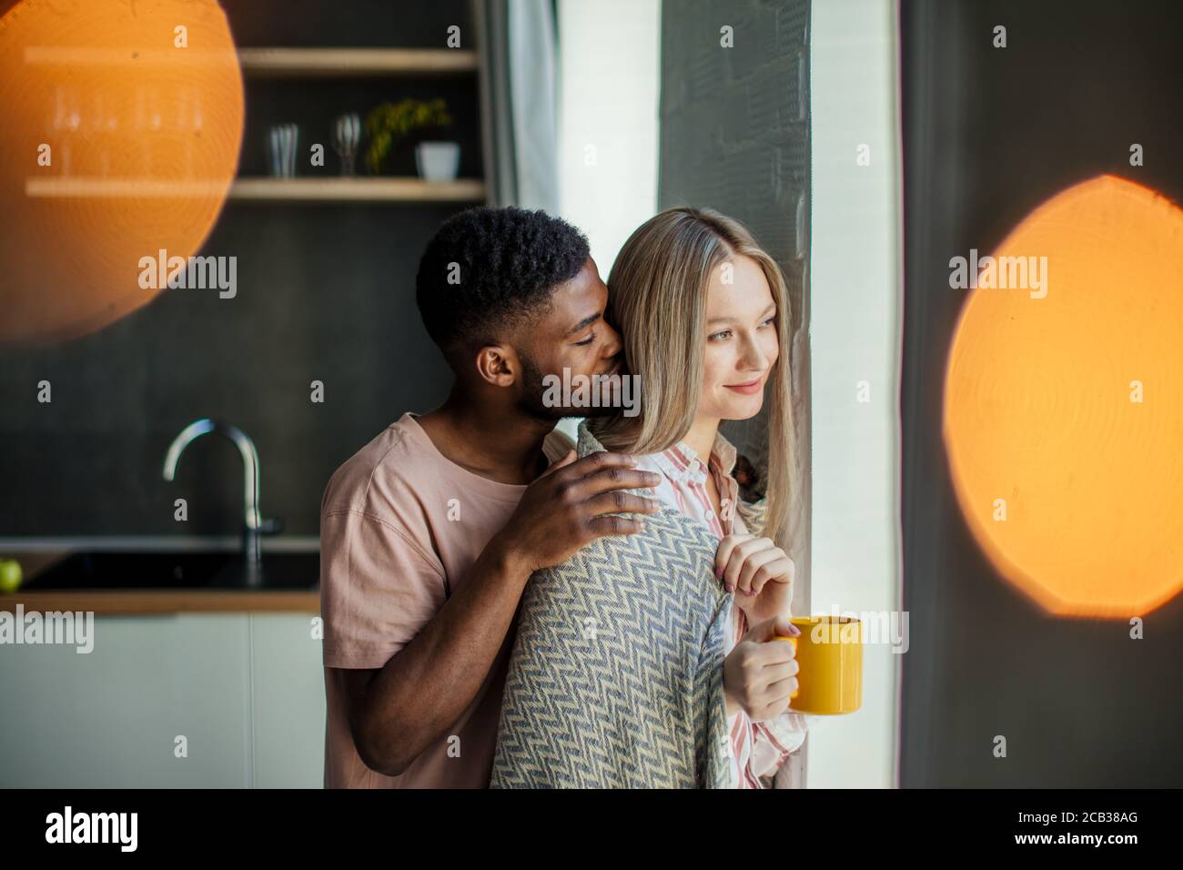 Schönen afrikanischen Kerl küsst seine kaukasischen Freundin am Hals von hinten, zu Hause in der Küche Zimmer mit modernem Interieur Stockfoto