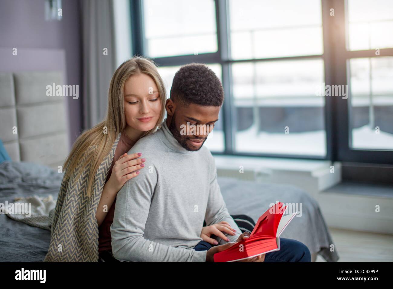 Die schöne Zeit zu Hause. Interracial attraktive Paar junge Leute kleben auf Bett, während Frau umarmt von der Rückseite einer Afrikanischen ma Stockfoto