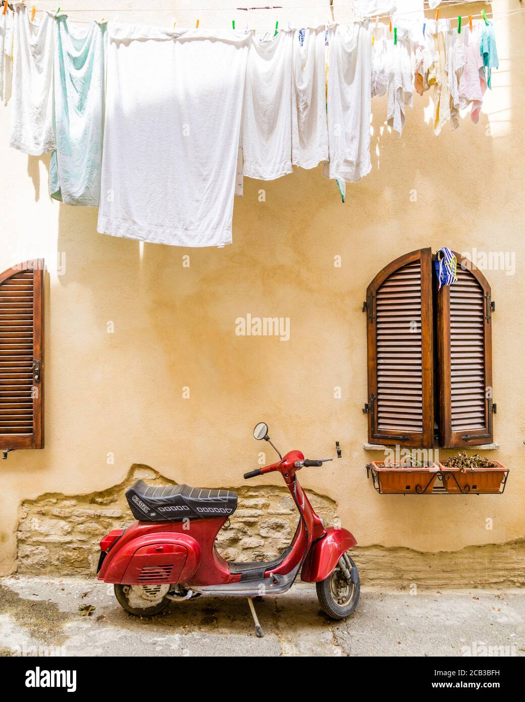 Ein roter Roller unter einer Wäscheleine in einer Straße in Bevagna, Umbrien, Italien geparkt Stockfoto