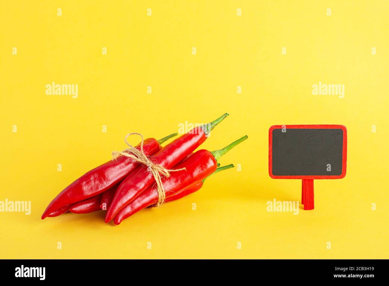 Rote scharfe Chilischote und eine kleine Tafel auf gelbem Hintergrund. Stockfoto