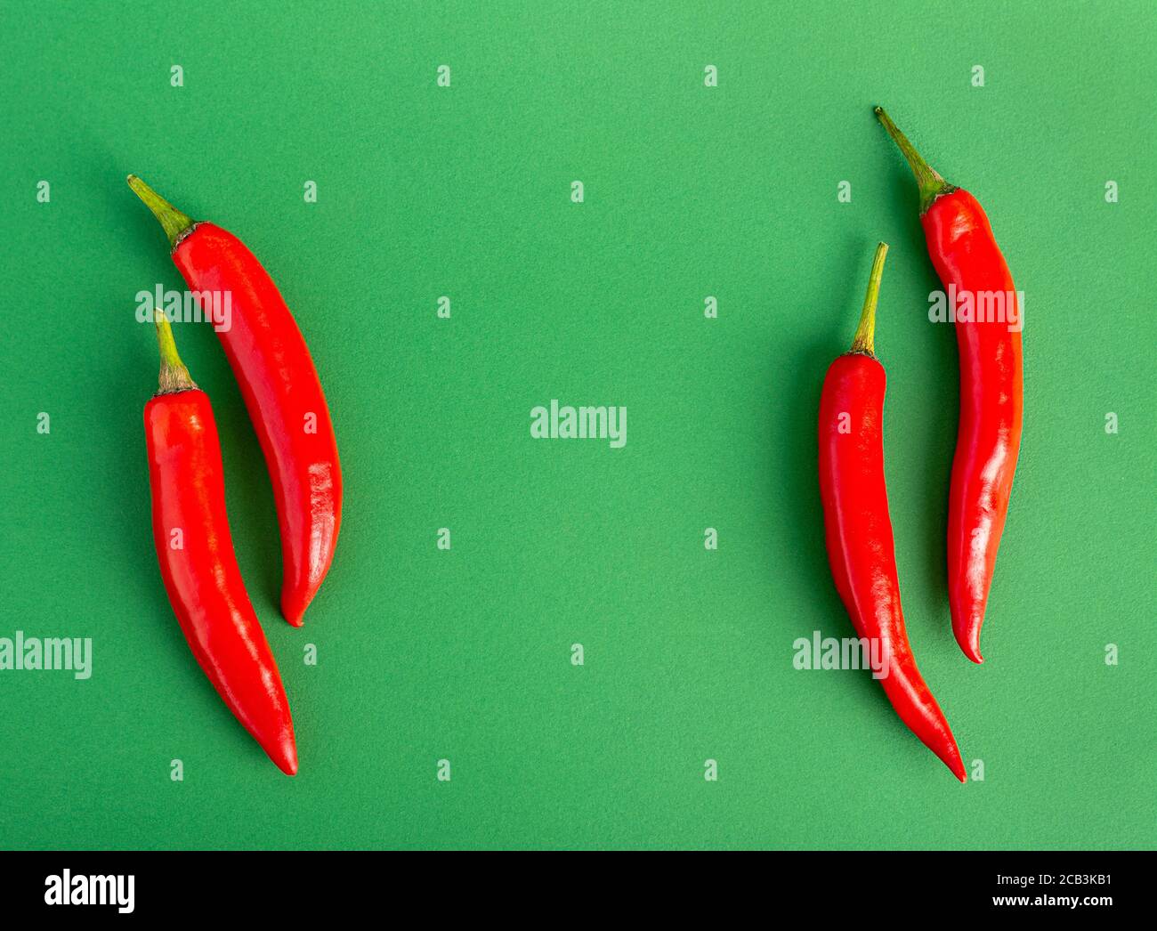Vier rote Chili-Paprika liegen auf jeder Seite Ein grüner Hintergrund Stockfoto