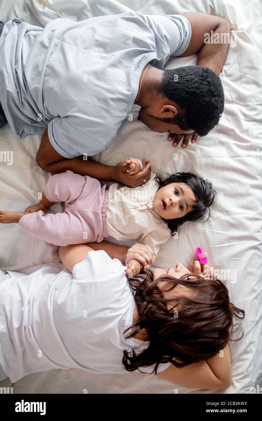 Müde Eltern schlafen auf dem Bett, während ihr Kind aufwacht, Draufsicht Foto. Familienleben Stockfoto