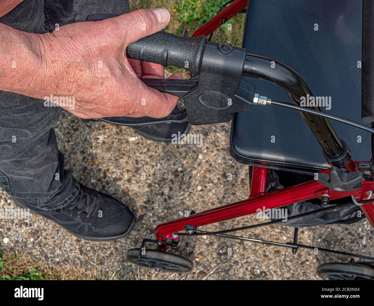 Nahaufnahme eines älteren Mannes, der mit seiner rechten Hand den rechten Seitengriff und die Bremse eines Erwachsenen-Kinderwagens/Rollators hält. Stockfoto