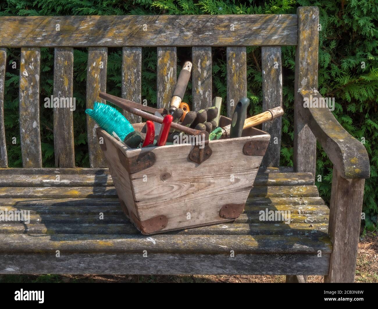 Nahaufnahme eines alten hölzernen Gartengerätebox, mit einer Vielzahl von Gartengeräten, auf einer alten Holzbank, in einem Garten / Hof, in der Sonne. Stockfoto