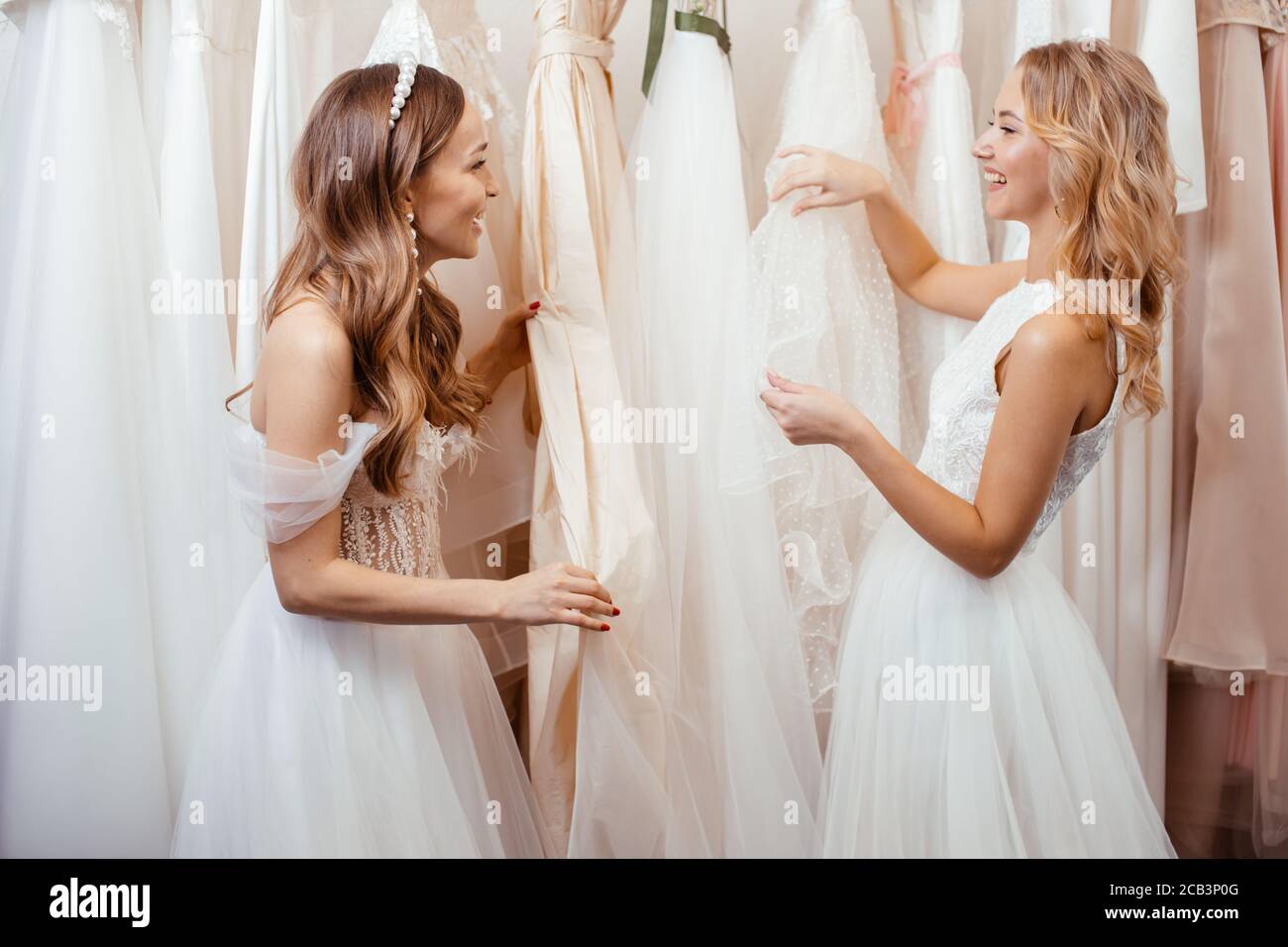 Junge kaukasische Freunde wählen, versuchen auf Hochzeitskleider im Salon, schöne Frauen für die Hochzeit vorbereiten, zu feiern, träumen Braut zu sein Stockfoto