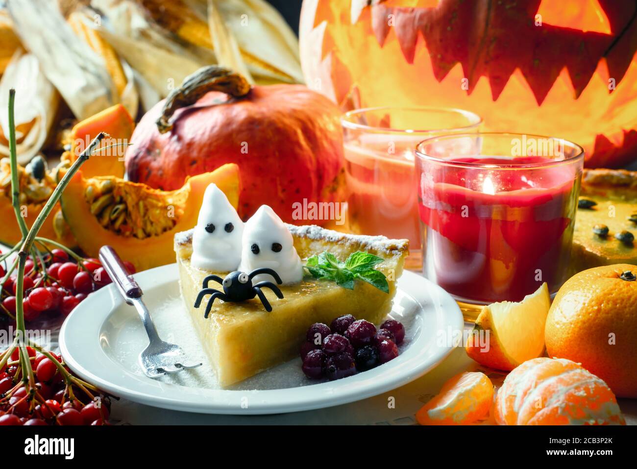 Leckere süße hausgemachte halloween Kürbiskuchen mit schwarzer Spinne und kleinen Geistern auf weißem Teller Nahaufnahme. Kerzen und Jack-o-Laterne auf dem Hintergrund. Traditionelles Urlaubsessen Stockfoto