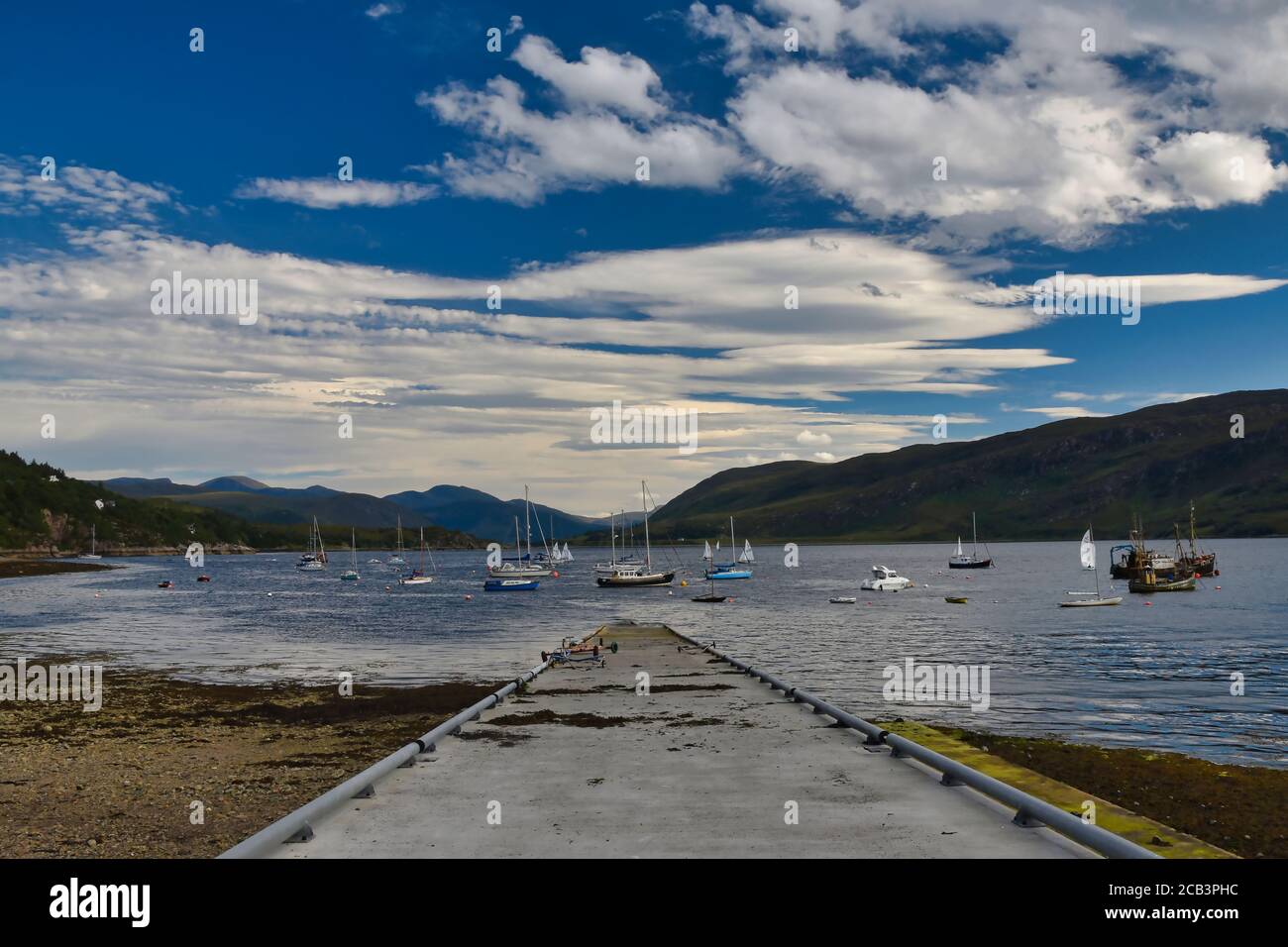 Ullapool Steg, Meer, Segelboote und Berge in schottischen Highlands an der Nordküste 500 Route an sonnigen Sommertagen mit blauem Himmel und Wolken Stockfoto