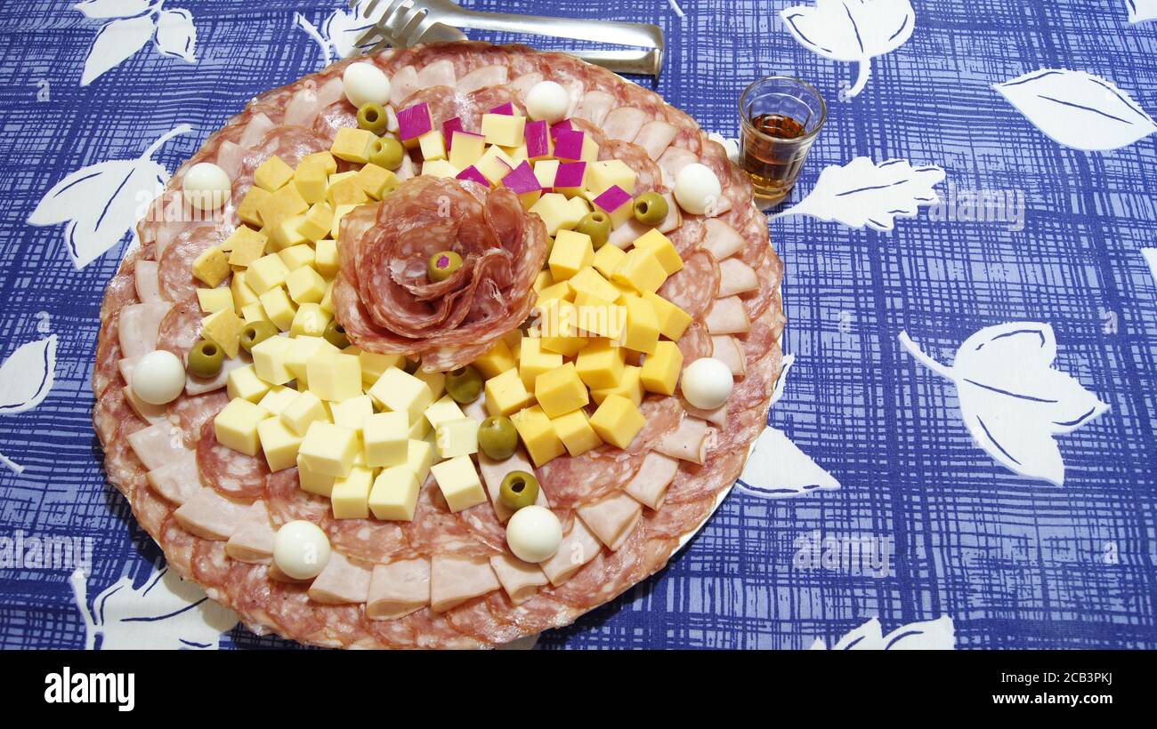 Weißes Gericht mit Salami, Schinken, Wachteleiern und Palmenherz, auf einem Hintergrund mit einer blau-weißen Tischdecke und einem Griff aus Whiskey-Glas Stockfoto