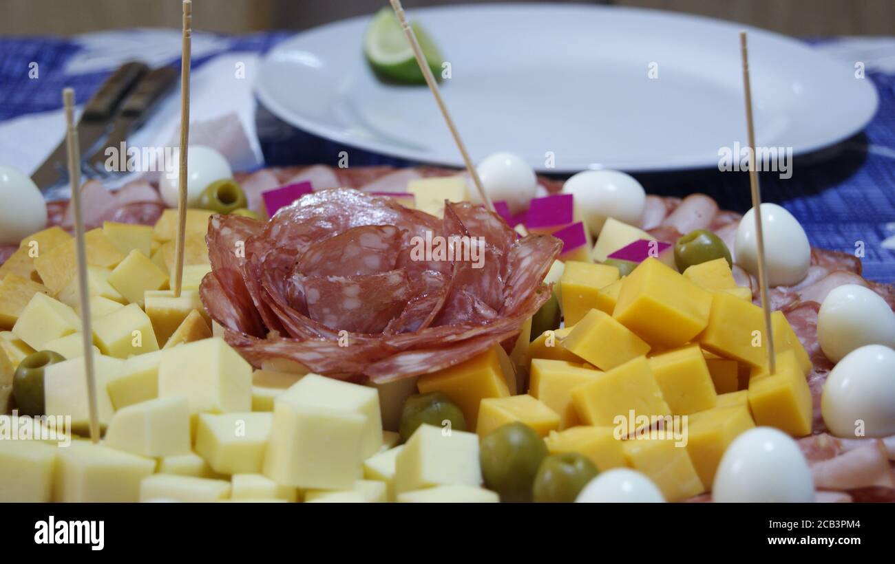Gerichte mit Wachteleiern verschiedene Arten von Käse Salami truthahn Fleisch grüne Oliven Sticks zu dienen und weiße Schale mit Zitrone aus Fokus auf blau Stockfoto