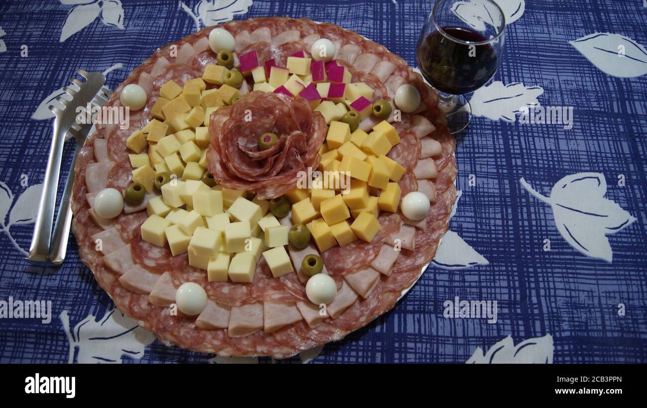 Weißer Teller mit Salami, Schinken, Wachteleiern und Palmenherz in der Mitte auf einem Hintergrund mit blauer und weißer Tischdecke, mit tong und Wein Stockfoto