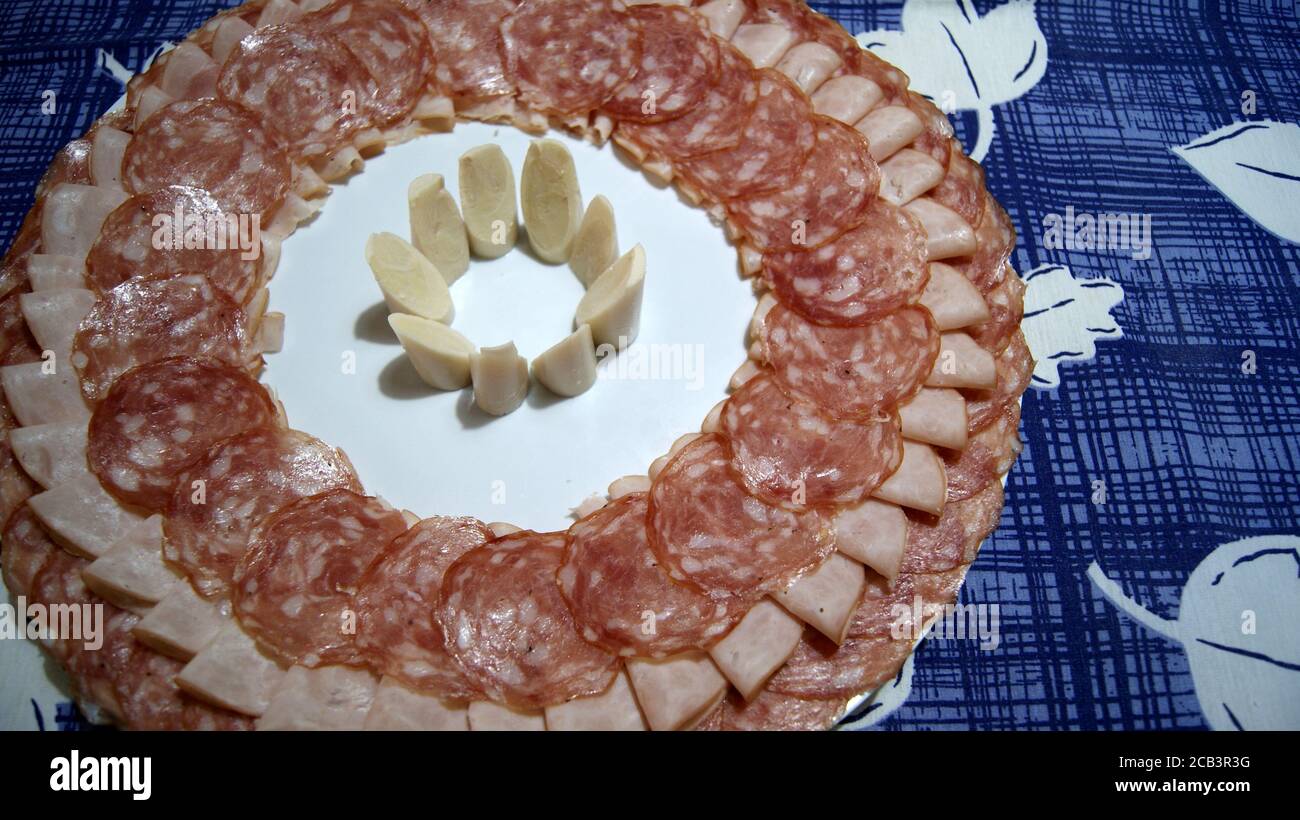 Weißes Gericht mit Salami, Schinken und Palmenherz in der Mitte auf einem Hintergrund mit einer blau-weißen Tischdecke verziert, Blick von oben, ein Gericht bekannt Stockfoto