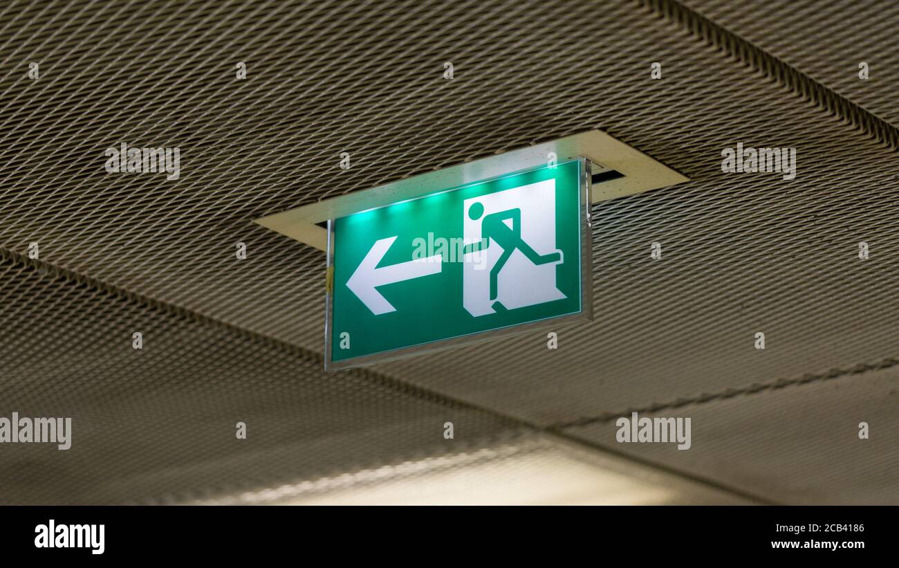 Beleuchtetes Notausgangsschild. Grünes Schild mit weißem Pfeil und nach links laufender Figur. Symbol für Flucht, weglaufen. Stockfoto